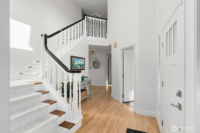 stairway with a towering ceiling, wood finished floors, and baseboards