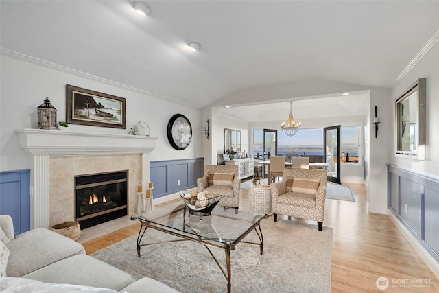 living room with a chandelier, light wood-style floors, lofted ceiling, crown molding, and a high end fireplace