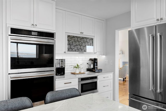 kitchen featuring appliances with stainless steel finishes, backsplash, white cabinetry, and light wood-style flooring