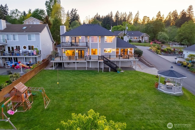 back of property at dusk featuring a gazebo, stairs, a yard, a deck, and a balcony