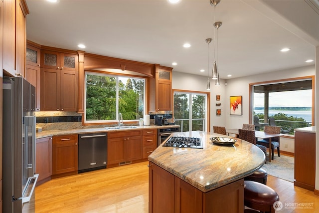kitchen with light wood-style flooring, brown cabinetry, a sink, a kitchen breakfast bar, and stainless steel appliances