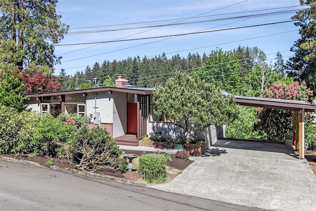 mid-century modern home with brick siding, driveway, a chimney, and a carport