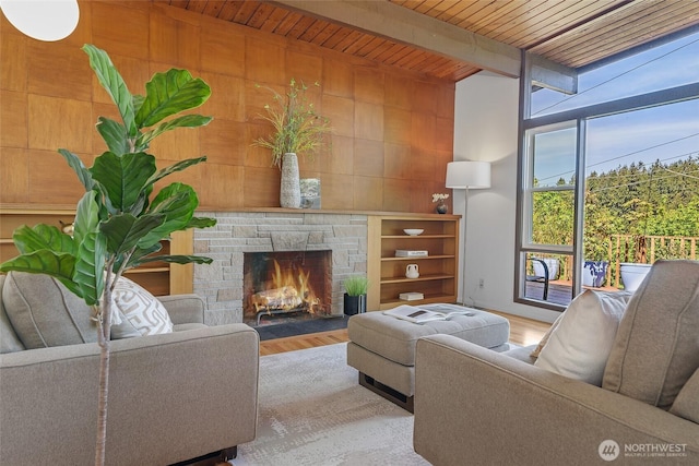 living area with wooden ceiling, a stone fireplace, wood finished floors, beamed ceiling, and wooden walls