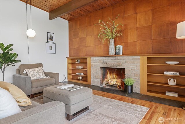 living area featuring wood ceiling, wood finished floors, beamed ceiling, and a stone fireplace