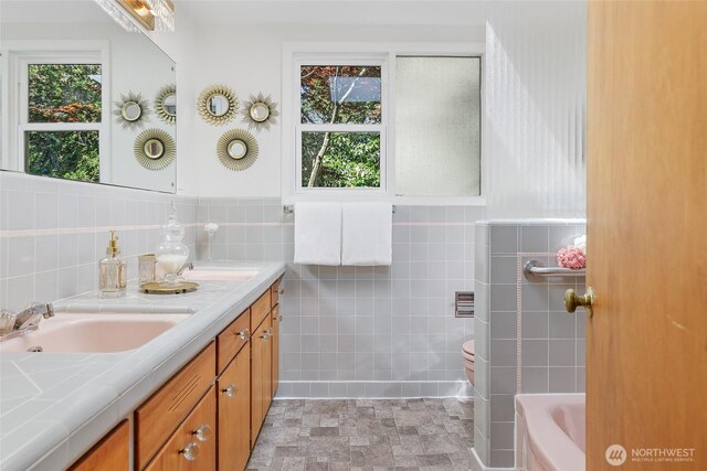 bathroom with tile walls, double vanity, and a tub