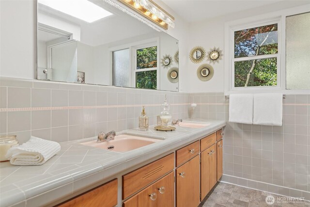 full bathroom with double vanity, tile walls, and a wainscoted wall