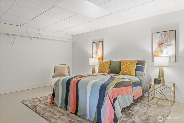 bedroom with baseboards, a paneled ceiling, and concrete flooring