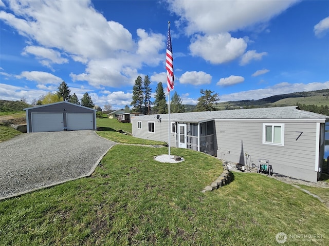 back of house with an outdoor structure, a detached garage, a yard, and a sunroom