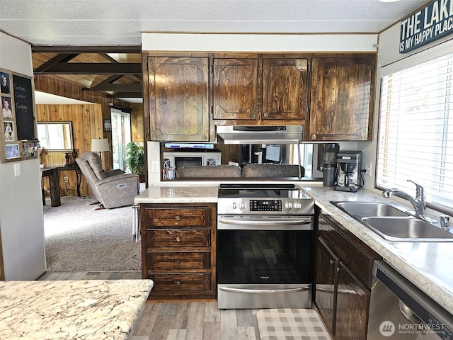 kitchen featuring vaulted ceiling with beams, under cabinet range hood, appliances with stainless steel finishes, light countertops, and a sink