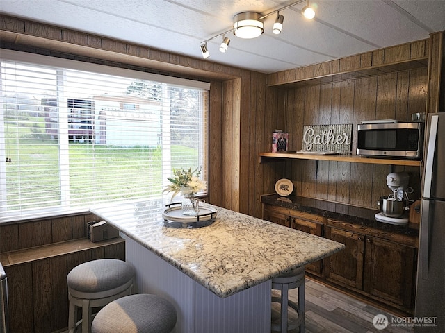 kitchen featuring a breakfast bar area, stainless steel appliances, open shelves, a wealth of natural light, and dark wood-style flooring