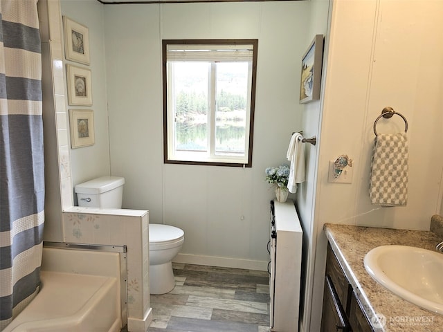 full bathroom with wood finished floors, a shower with curtain, toilet, vanity, and baseboards