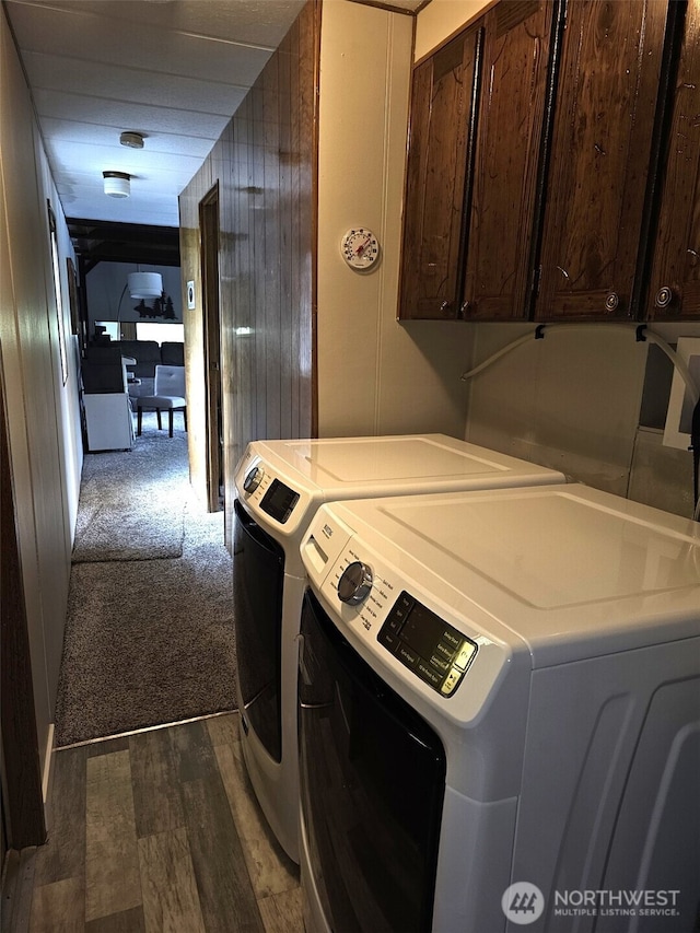 clothes washing area featuring wooden walls, dark wood-style floors, cabinet space, and washer and clothes dryer