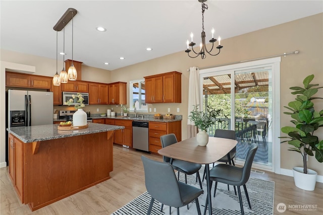 kitchen with a center island, brown cabinets, light wood finished floors, a chandelier, and stainless steel appliances