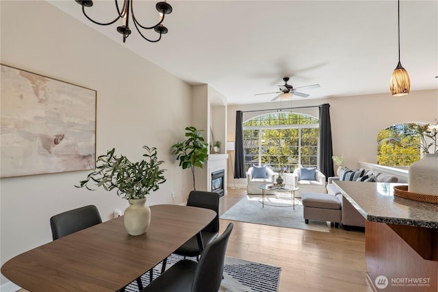 dining space featuring a glass covered fireplace, ceiling fan with notable chandelier, and light wood finished floors