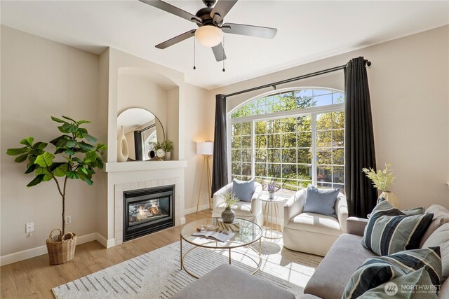 living area with baseboards, ceiling fan, a fireplace, and wood finished floors