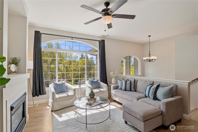 living area featuring light wood-style floors, baseboards, ceiling fan with notable chandelier, and a tile fireplace