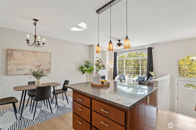 kitchen with light wood-style floors, a center island, dark stone counters, brown cabinets, and a notable chandelier