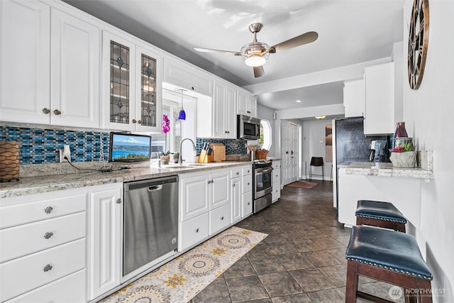 kitchen with white cabinets, stainless steel appliances, a sink, glass insert cabinets, and tasteful backsplash