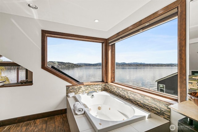 bathroom featuring wood finished floors, a water view, a jetted tub, baseboards, and recessed lighting