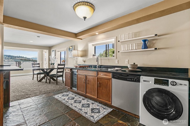 kitchen featuring stone tile floors, stainless steel dishwasher, a sink, and washer / clothes dryer