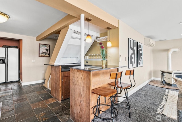 kitchen with a wall mounted air conditioner, white refrigerator with ice dispenser, a wood stove, baseboards, and a peninsula
