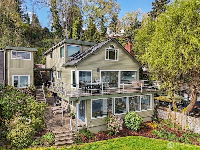 rear view of property with a deck, a chimney, stairway, and fence
