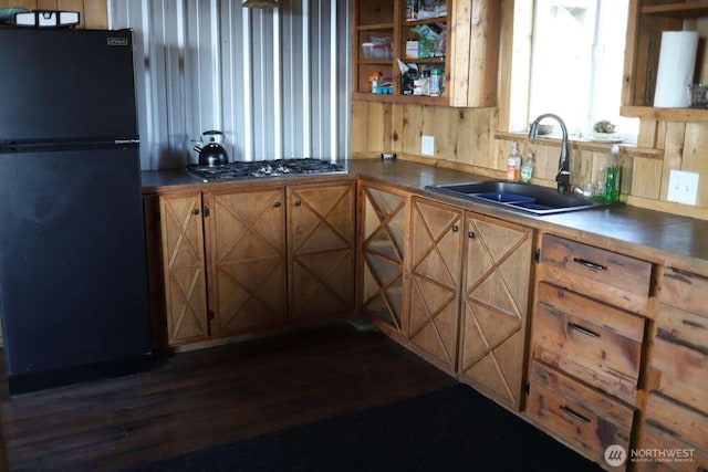 kitchen featuring a sink, stainless steel gas cooktop, brown cabinetry, dark wood-type flooring, and freestanding refrigerator