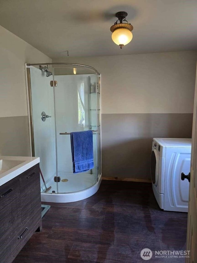 bathroom with a shower stall, wood finished floors, vanity, washer / dryer, and baseboards