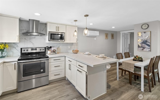 4204 Letitia Ave S, Seattle, WA 98118 - kitchen with light wood finished floors, a peninsula, wall chimney exhaust hood, white cabinets, and appliances with stainless steel finishes