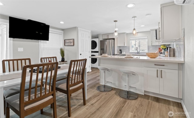 4204 Letitia Ave S, Seattle, WA 98118 - kitchen featuring a peninsula, freestanding refrigerator, stacked washer / drying machine, light wood-type flooring, and backsplash