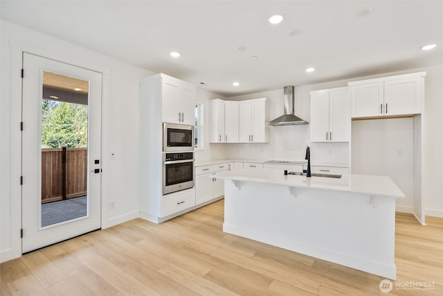 9705 205th St E Unit 29, Graham, WA 98338 - kitchen with light wood-style floors, light countertops, wall chimney exhaust hood, a sink, and stainless steel appliances