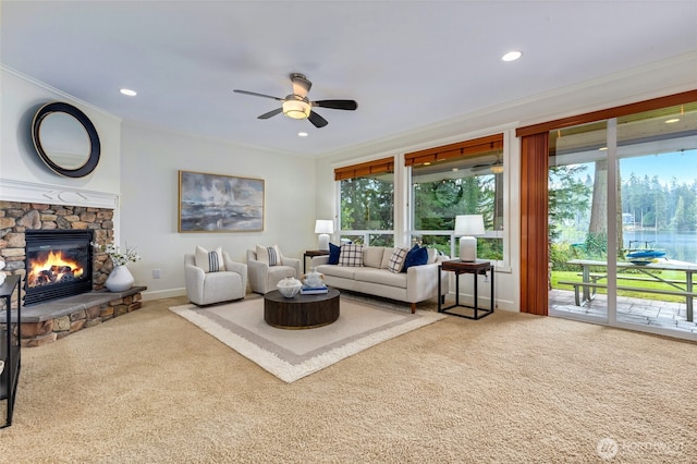 carpeted living room featuring plenty of natural light, a stone fireplace, ornamental molding, and ceiling fan