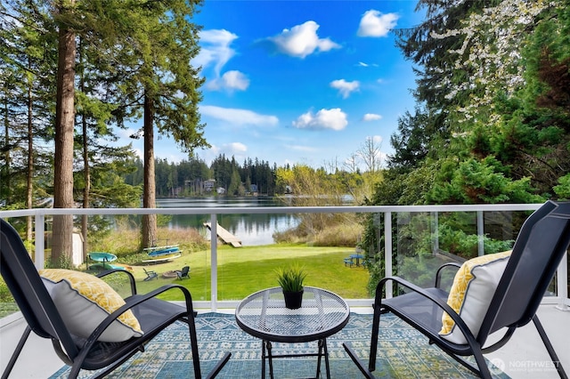balcony with a water view, a view of trees, and a patio