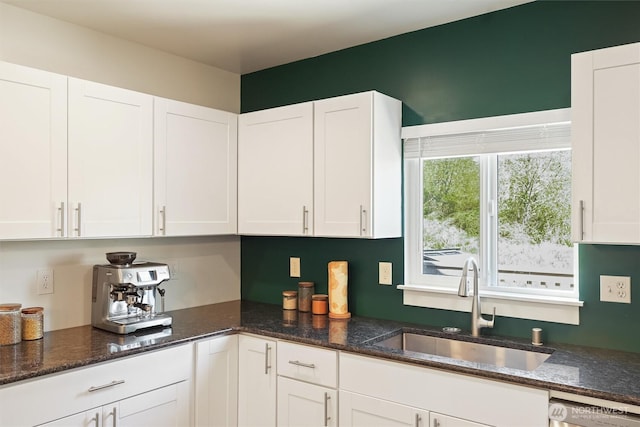 kitchen featuring dark stone countertops, dishwashing machine, white cabinetry, and a sink