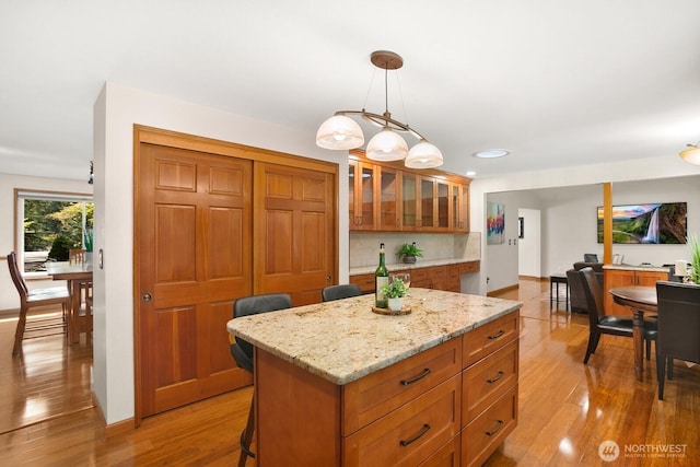 kitchen featuring brown cabinets, hanging light fixtures, light wood finished floors, a center island, and glass insert cabinets