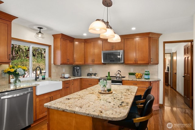 kitchen featuring a breakfast bar area, backsplash, wood finished floors, a sink, and stainless steel appliances