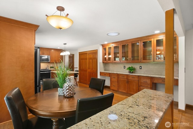 kitchen with decorative backsplash, light wood-type flooring, brown cabinets, glass insert cabinets, and stainless steel appliances