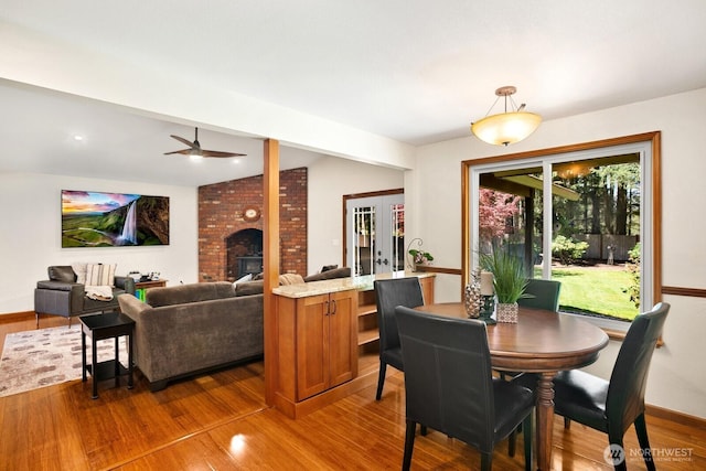 dining room featuring french doors, a ceiling fan, a brick fireplace, wood finished floors, and baseboards