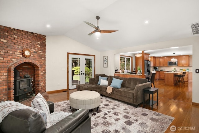 living area featuring ceiling fan, french doors, visible vents, a wood stove, and wood finished floors