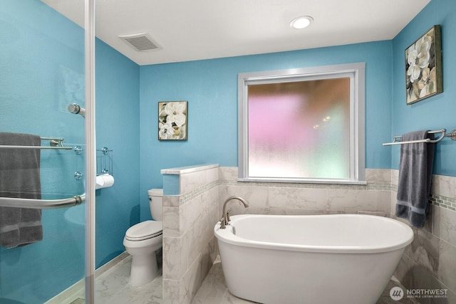 full bath featuring visible vents, a freestanding tub, tile walls, wainscoting, and toilet