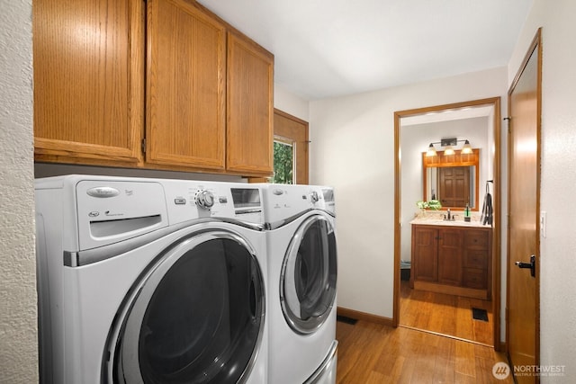 laundry area with washing machine and clothes dryer, a sink, light wood-style flooring, and cabinet space