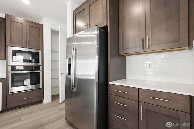 20519 97th Ave E Unit 26, Graham, WA 98338 - kitchen featuring appliances with stainless steel finishes, backsplash, light wood-style flooring, light countertops, and dark brown cabinetry