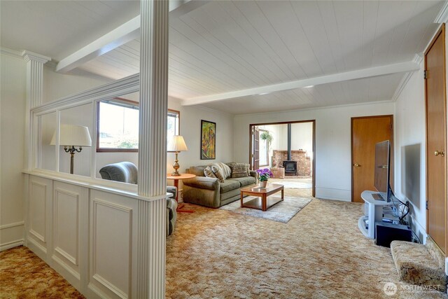living area with ornate columns, beamed ceiling, a wood stove, and carpet floors