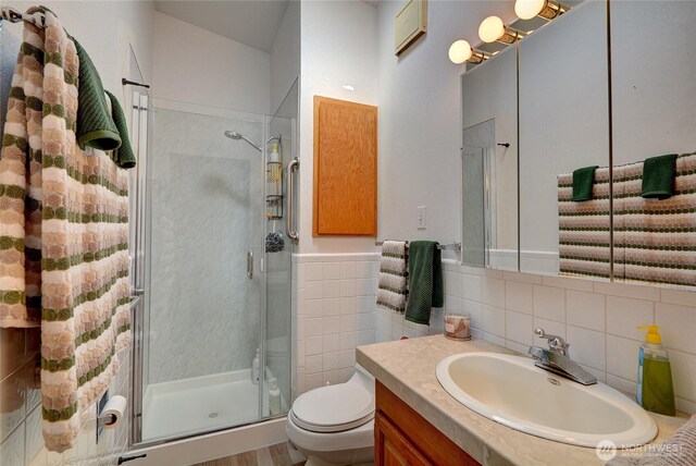bathroom with vanity, toilet, a stall shower, and tile walls