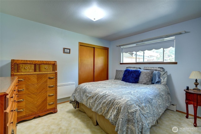 bedroom with a baseboard heating unit, a closet, light colored carpet, and baseboards