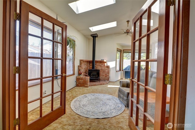 interior space with a wood stove, carpet floors, lofted ceiling with skylight, french doors, and a ceiling fan