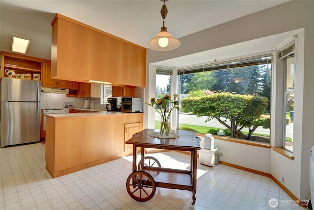 kitchen with freestanding refrigerator, under cabinet range hood, stove, a peninsula, and backsplash