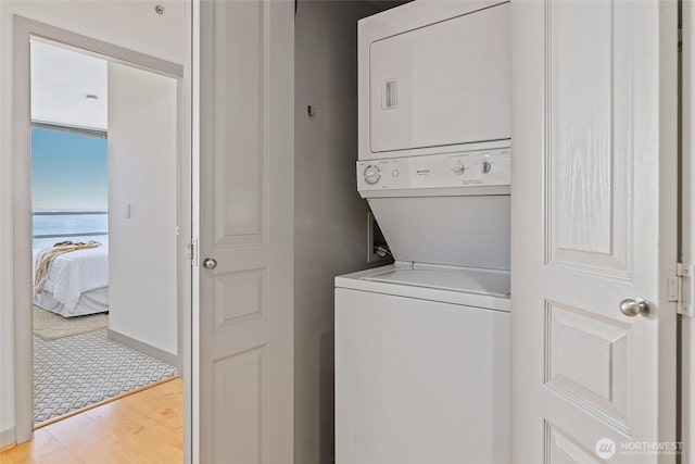 clothes washing area featuring a water view, stacked washer / dryer, laundry area, and wood finished floors