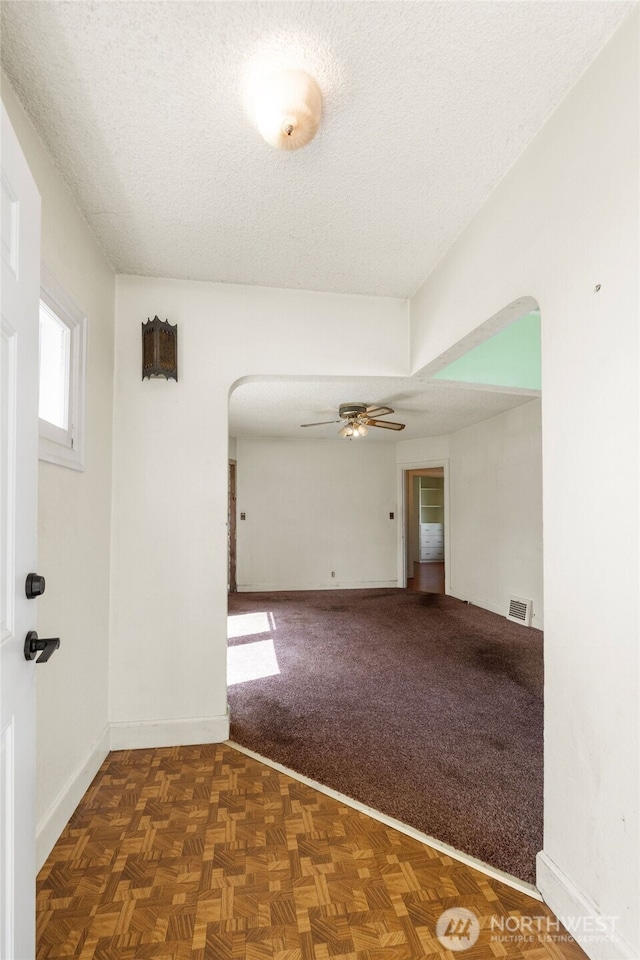 spare room featuring visible vents, arched walkways, baseboards, a textured ceiling, and ceiling fan
