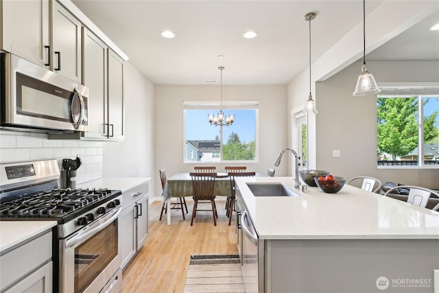 kitchen featuring light wood finished floors, stainless steel appliances, a sink, recessed lighting, and decorative backsplash